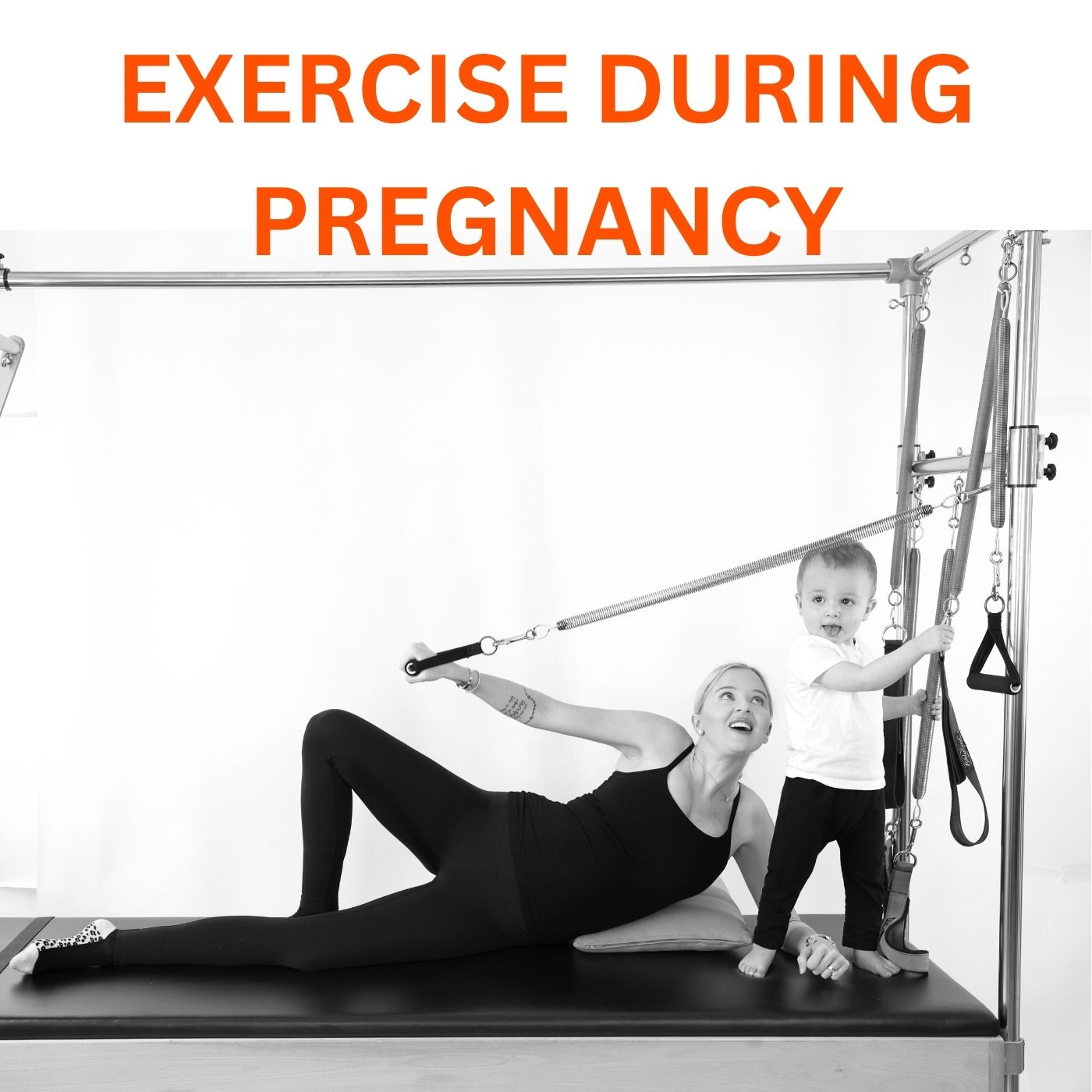 Pregnant woman exercising on the Pilates Cadillac doing side lying arm springs. Her 2 year old son is close by holding an arm spring handle